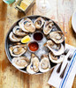 Freshly Shucked Oysters (Pint), raw oysters served on a bed of ice in a round metal tray with lemon wedges and dipping sauces on the side.