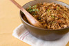 Broussard's Bayou Broussards Bayou Company Cornbread Dressing 32oz, close-up of seasoned cornbread dressing in a bowl with herbs and a wooden spoon, on a white cloth napkin.