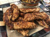 Ragin Cajun 8oz Chicken or Gator Cajun Seasoning & Rub, seasoned and grilled chicken wings with a seasoned spice crust served on a black and cream platter.