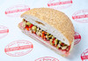 Central Grocery’s Original & Hot Olive Salad Combo 16oz – Authentic New Orleans Taste, a sandwich with bread, olive salad, cheese, and ham, on branded paper.