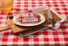 The Best Stop Original Boudin 14oz, packaged sausage product on a baking sheet with a knife, on a red and white checkered tablecloth.