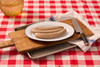 The Best Stop Mild Boudin 16oz, uncooked sausages on a white plate, placed on a wooden cutting board with a knife, set on a red and white checkered tablecloth.