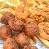 Louisiana Fish Fry Hush Puppy Mix 7.5oz, cooked hush puppies with a golden brown crispy exterior served with French fries and lemon wedges.
