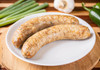 La Boucherie Cajun Style Boudin 16oz, cooked sausage links on a white plate with green onions, garlic, and a green pepper in the background.