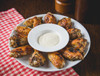La Boucherie Chicken Hot Wings 24 oz, crispy grilled chicken wings with a side of creamy dipping sauce, served on a white plate with a red checkered napkin.