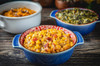 La Boucherie Smothered Corn 1lb, flavorful cooked corn dish with bacon bits served in a colorful bowl on a rustic wooden table.