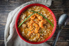 La Boucherie Crawfish Étouffée 1.75lb, served in a red bowl with crawfish and rice, garnished with green onions on a rustic wooden table.