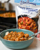 Blue Runner Sauce Piquante 30oz Pouch, a bag of spicy Cajun seafood sauce used for cooking, with a bowl of cooked chicken and rice topped with the sauce on a white table.