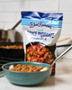 Blue Runner Sauce Piquante 30oz Pouch, image of a package of Cajun-seasoned simmering sauce standing next to a bowl of prepared dish with sauce on a kitchen counter.