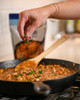 Blue Runner Cajun Fricassee 30oz Pouch, a person garnishing a freshly cooked Cajun dish with chopped parsley in a black skillet.