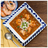 Blue Runner Shrimp Creole Base 25oz, savory shrimp creole sauce served in a white bowl garnished with chopped green onions on top, alongside cooked shrimp on a blue patterned plate.
