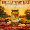 Cajun Chef Mild Pickled Okra 12oz, glass jar filled with pickled okra opposite a sunset scene with a Louisiana theme, surrounded by charcuterie, cheese, olives, and crackers on a wooden table.