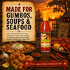 Cajun Chef Louisiana Hot Sauce 6oz bottle, red hot sauce in a clear glass bottle with a yellow cap with red text, surrounded by Cajun seafood, rice, corn, garlic, chili peppers, and spices in a rustic outdoor setting at sunset.