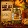 Cajun Chef Spicy Green Beans 32oz, jar of seasoned green beans with Louisiana spices, surrounded by crackers, olives, and a drink with celery and lemon slices on a rustic background at sunset.