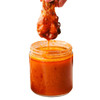 Cajun Chef Wing Sauce 128oz, hot wing sauce being dipped from a chicken wing into a glass jar filled with spicy orange wing sauce.