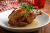 Poche's Stuffed Chicken w/ Spinach Madeline 3lb, cooked roasted chicken garnished with fresh herbs on a white plate.