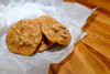 Poche's Pecan Pralines, close-up of two golden-brown pecan pralines with chopped pecans on top, resting on crinkled white parchment paper on a wooden surface.