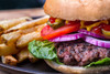JV Foods Wagyu 5lb Ground Meat, close-up of a juicy hamburger with lettuce, tomato, onions, pickles, and condiments in a bun, served with fries.