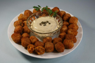 Cajun Original Crawfish Bites 1lb (26 Bites), golden fried crawfish bites served with creamy dipping sauce in a glass bowl, garnished with parsley on a white plate.