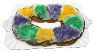 Creole Foods of Louisiana Praline Cream Cheese King Cake with icing on side, decorated with green, purple, and yellow colored sugar, and a small gold figurine on top, served on a white platter.