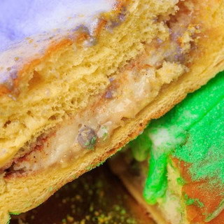 Gambino's Bavarian King Cake with icing on side, close-up view of the moist, layered cake filled with creamy filling and colorful icing decoration.