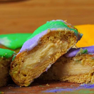 Gambino's Cream Cheese King Cake with icing on side, featuring vibrant purple, green, and yellow icing on a traditional king cake with creamy filling inside.
