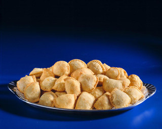 Mrs Wheat's Mini Crawfish Pies 100ct 1oz, a platter of bite-sized, golden-brown savory crawfish pies on a decorative silver tray against a deep blue background.