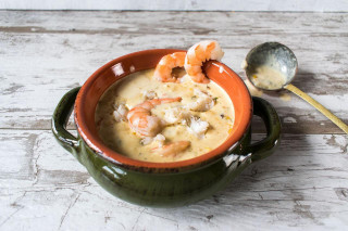Ragin Cajun Authentic Seafood Bisque 10 oz - Food Service, creamy seafood bisque with shrimp and crab, served in a rustic ceramic bowl on a wooden surface with a seafood ladle beside it.