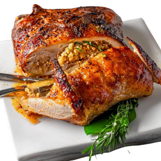 Creole Foods of Louisiana Creole Pork & Cornbread Turducken 15lbs (Serves approximately 20-25), a roasted turducken with crispy, seasoned exterior, sliced to reveal layers of pork, cornbread stuffing, and poultry, served on a white plate with herbs.