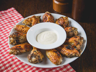 La Boucherie Chicken Hot Wings 24 oz, crispy grilled chicken wings with a side of creamy dipping sauce, served on a white plate with a red checkered napkin.