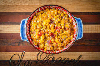 La Boucherie Smothered Corn 1lb, cooked creamy corn side dish with bacon bits in a decorative bowl.