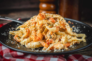 La Boucherie Crawfish Fettuccine Side Dish 2 lb, creamy pasta with crawfish, sprinkled with cheese and spices on a black plate.