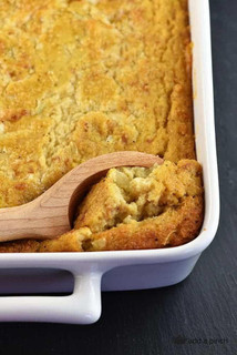 King Creole Cornbread Dressing 4lb, baked cornbread dressing in a white baking dish with a wooden spoon scooping a portion.