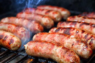 Poche's Poches Bridge Hot Sausage 3lb, grilled sausages cooking on a barbecue grill with visible grill marks and smoke.