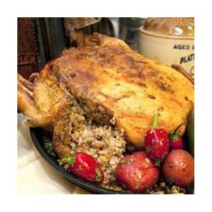 Comeaux's Stuffed Chicken with Crawfish 4lb, cooked, golden-brown stuffed chicken served with fresh strawberries and cherry tomatoes on a black plate.