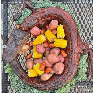 Creole Foods of Louisiana Whole Skinned Alligator Extra Large 20+ lbs, cooked alligator with corn, potatoes, and vegetables in a serving dish.