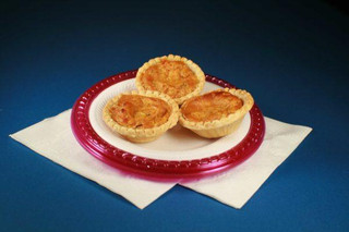 Cajun Original Crawfish Pies 4pk 3in, image of three cooked crawfish pies with golden crust on a red and white plate, placed on a white napkin against a dark blue background.