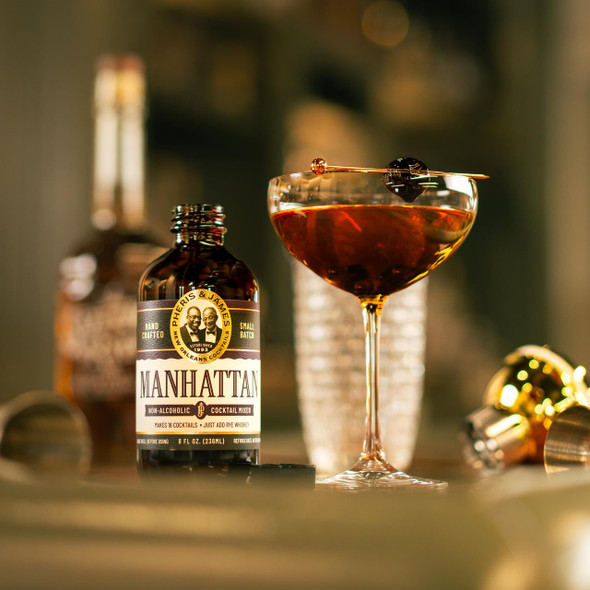 Pheris & James Manhattan Cocktail Mix - 8 fl oz, bottle of non-alcoholic cocktail mix with a finished Manhattan cocktail garnished with cherries in a cocktail glass.