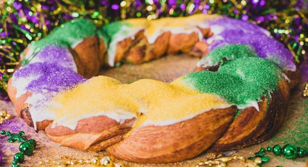 Creole Foods of Louisiana Traditional King Cake with icing on side, decorated with colorful sugar and surrounded by festive beads and decorations for Mardi Gras celebration.