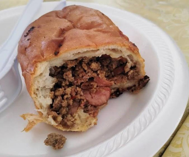 M&R Creole's Stuffed Pizza Bread 4ct, close-up of a sliced stuffed pizza bread showing meat, cheese, and sauce filling inside a golden-brown crust on a white plate.