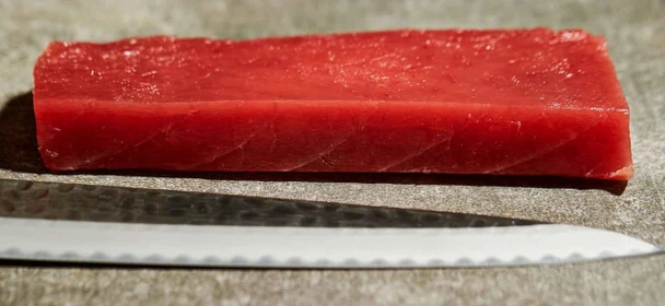 JV Foods Yellowfin Tuna Saku, fresh red tuna sashimi block on a cutting board with a knife.