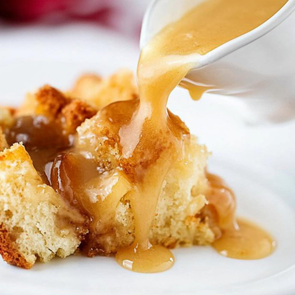 Carnival Bread Pudding Sauce 2lb, image of rich, golden bread pudding being topped with caramel sauce while served on a white plate.
