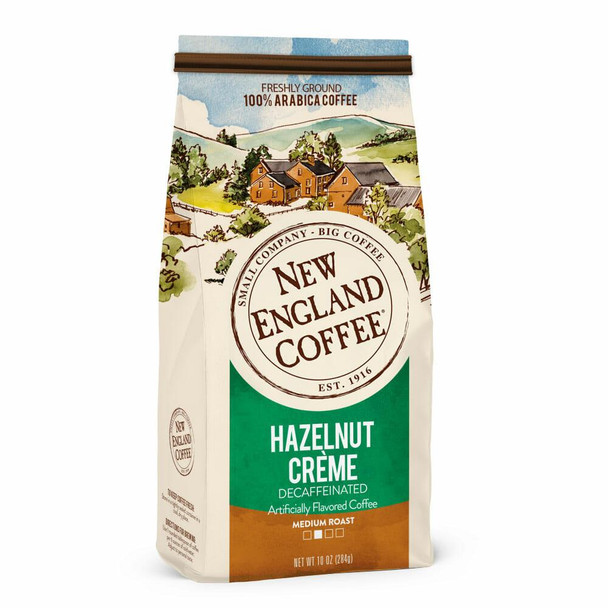 New England Coffee Hazelnut Creme Decaf Ground 10 oz, ground coffee package with illustrated countryside scene, featuring houses and hills, label indicating medium roast and decaffeinated flavor.