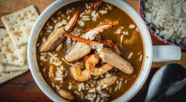 La Boucherie Seafood Gumbo 32 oz, a bowl of seafood gumbo with shrimp, crab, and fish in a rich broth, served with rice and saltine crackers.