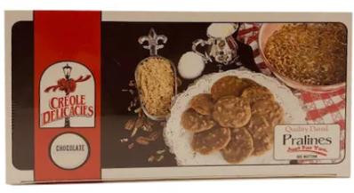 Creole Delicacies Chocolate Praline, assorted chocolate pralines displayed on a tray with a decorative gold spoon and a bowl of crushed nuts in the background