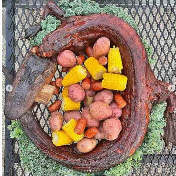 Creole Foods of Louisiana Whole Skinned Alligator Extra Large 20+ lbs, cooked alligator with corn, potatoes, and vegetables in a serving dish.