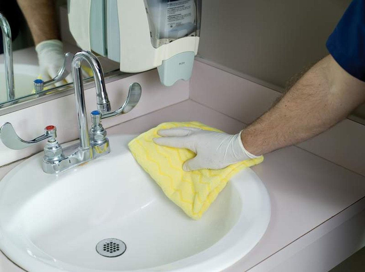 FGQ61000YL00 - Janitor wearing white rubber gloves wiping down a washroom sink with the HYGEN microfibre cloth