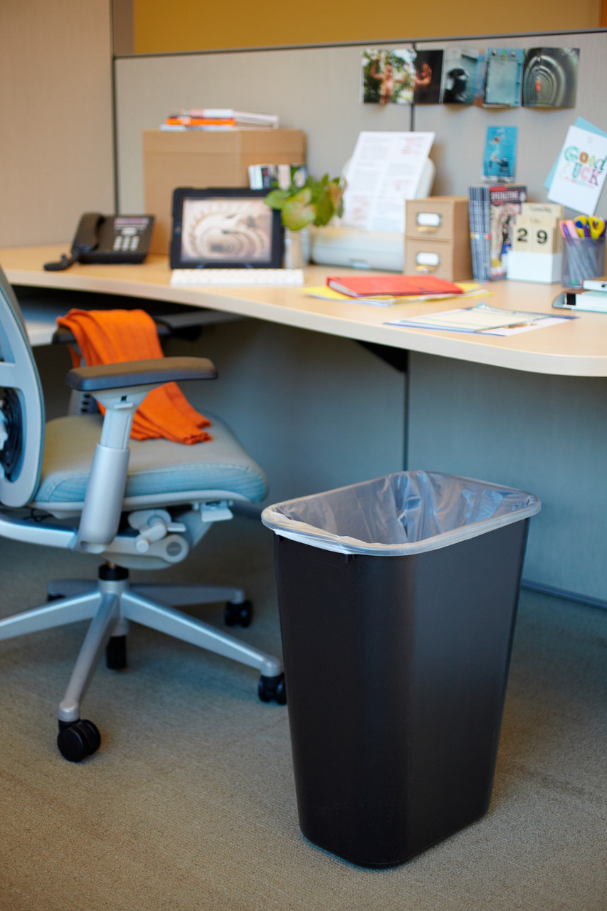 FG295700BLA - Black Rubbermaid wastebasket placed underneath a desk and fitted with a polythene bin liner