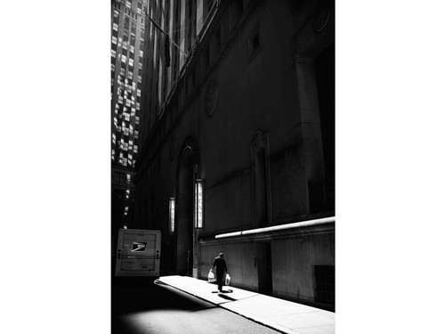 Person walking through a narrow urban corridor emphasizing light, shadow, and scale