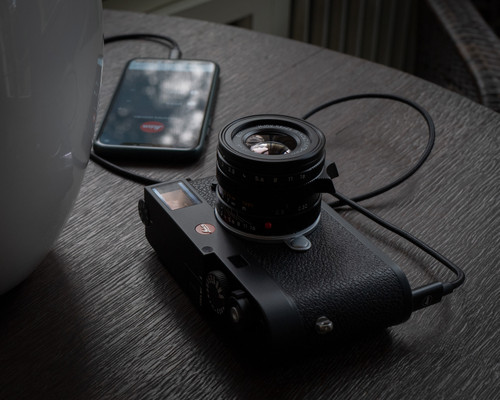 Leica M11 camera connected to smartphone via cable on tabletop